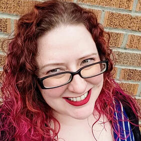 A smiling woman with glasses and pink hair